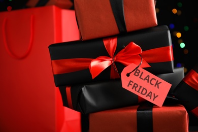 Gift boxes with Black Friday tag and shopping bag against blurred lights, closeup