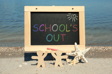 Image of Chalkboard with text SCHOOL'S OUT, wooden people and starfish on beach