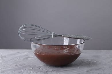 Photo of Whisk and bowl with chocolate cream on table against grey background