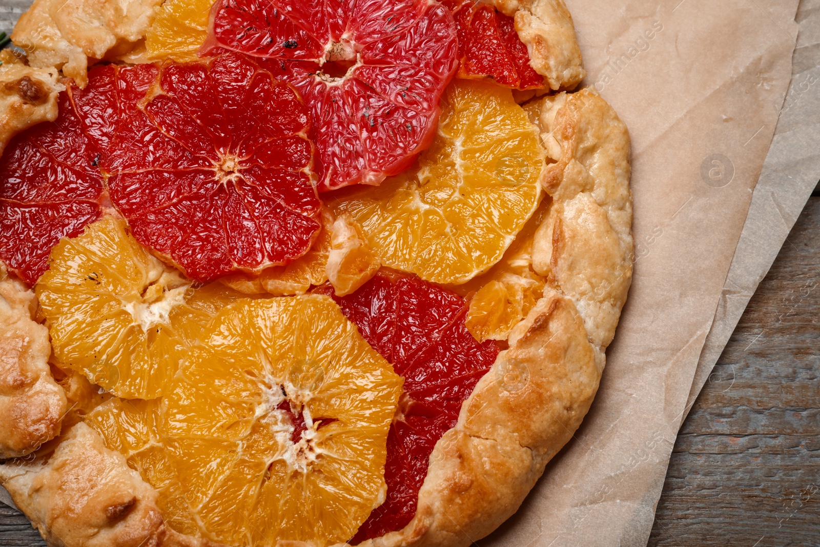 Photo of Delicious galette with citrus fruits on wooden table, closeup