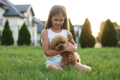 Photo of Beautiful girl with cute Maltipoo dog on green lawn in backyard