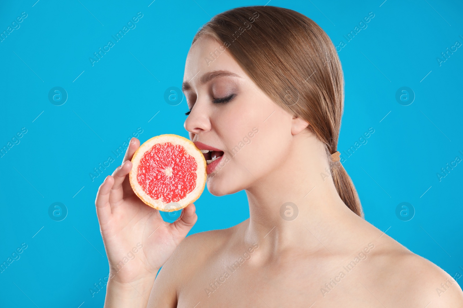 Photo of Young woman with cut grapefruit on blue background. Vitamin rich food