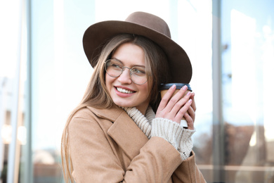 Photo of Young woman with cup of coffee on city street in morning