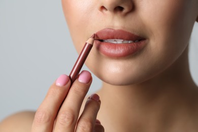 Photo of Young woman applying beautiful nude lip pencil on light grey background, closeup