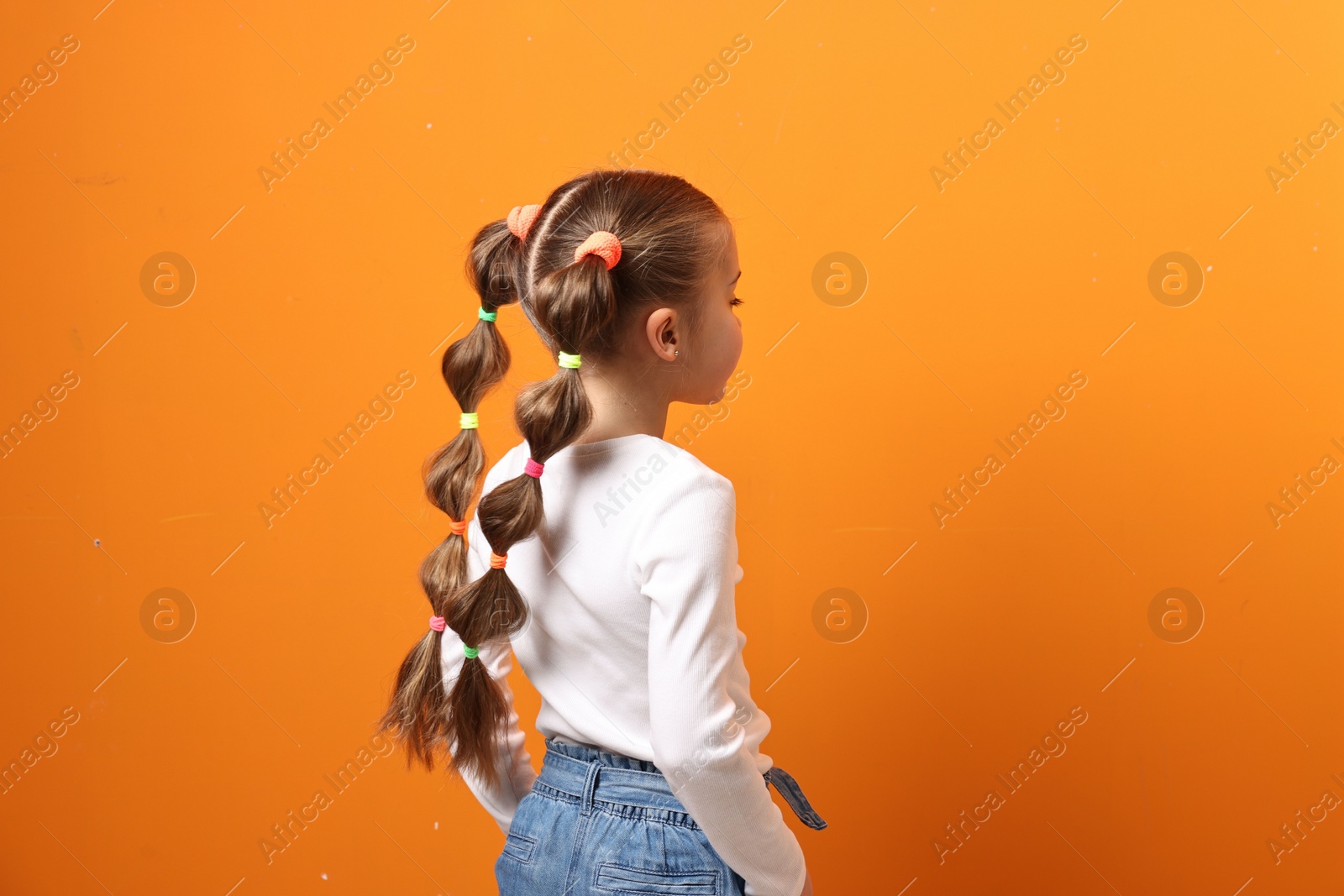 Photo of Cute little girl with beautiful hairstyle on orange background. Space for text