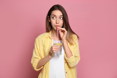 Young woman drinking lemon water on pink background