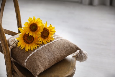 Bouquet of beautiful sunflowers and cushion on chair indoors. Space for text