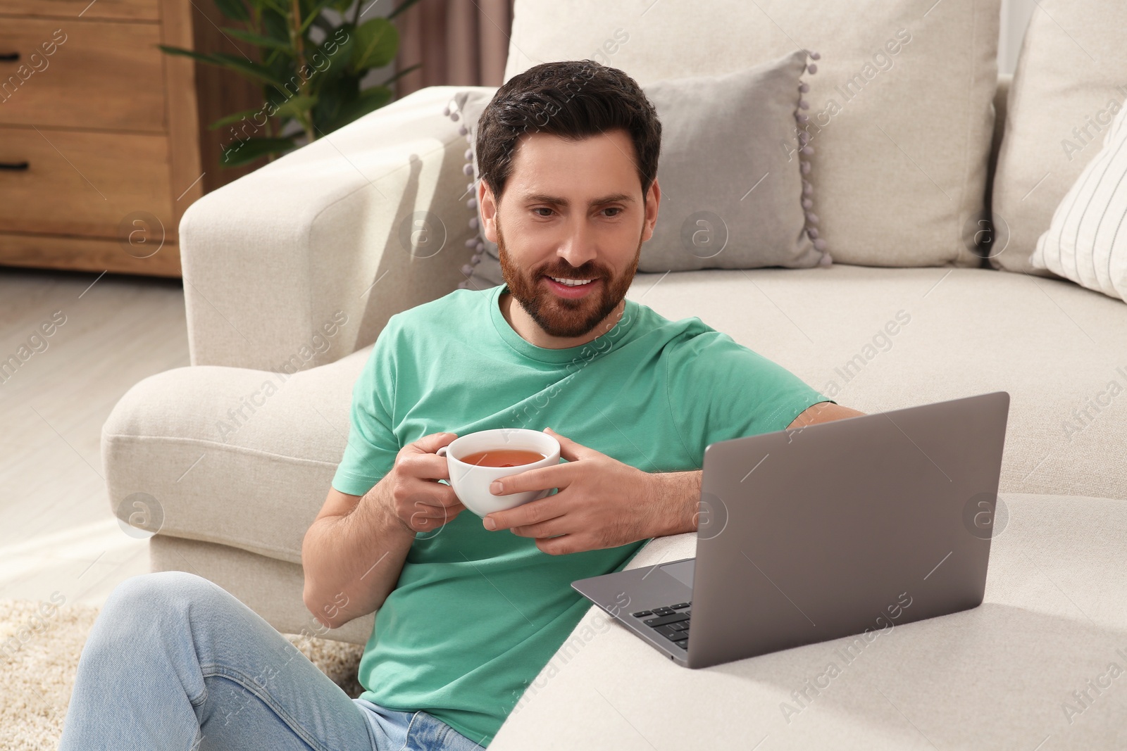 Photo of Man with cup of tea using laptop at home