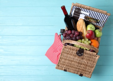 Photo of Wicker picnic basket with wine and different products on wooden table, top view. Space for text
