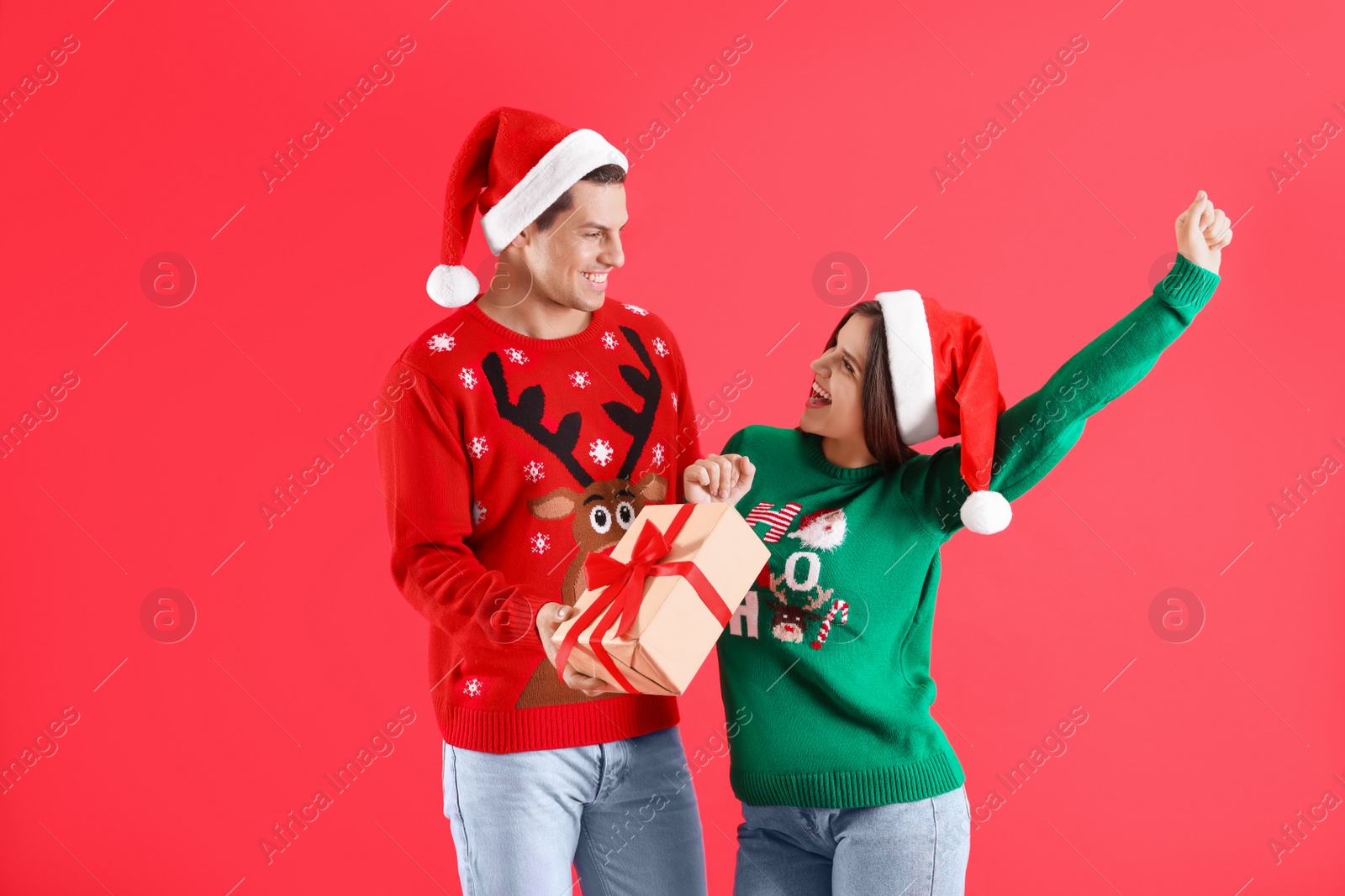 Photo of Man presenting Christmas gift to his girlfriend on red background