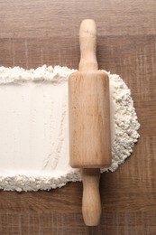 Photo of Flour and rolling pin on wooden table, top view