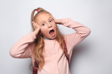 Emotional little girl with backpack on white background