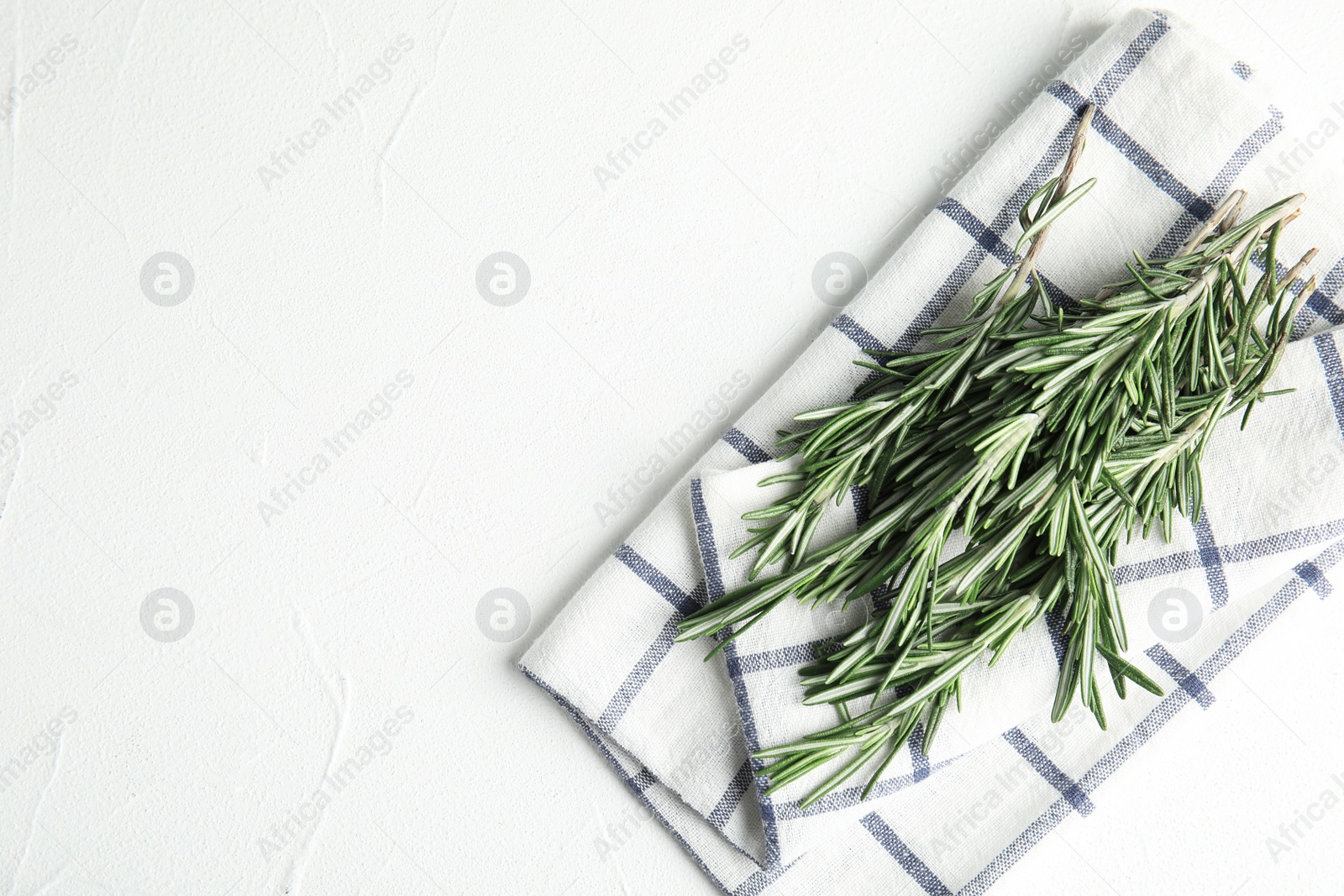 Photo of Fresh green rosemary and napkin on white table, top view. Space for text