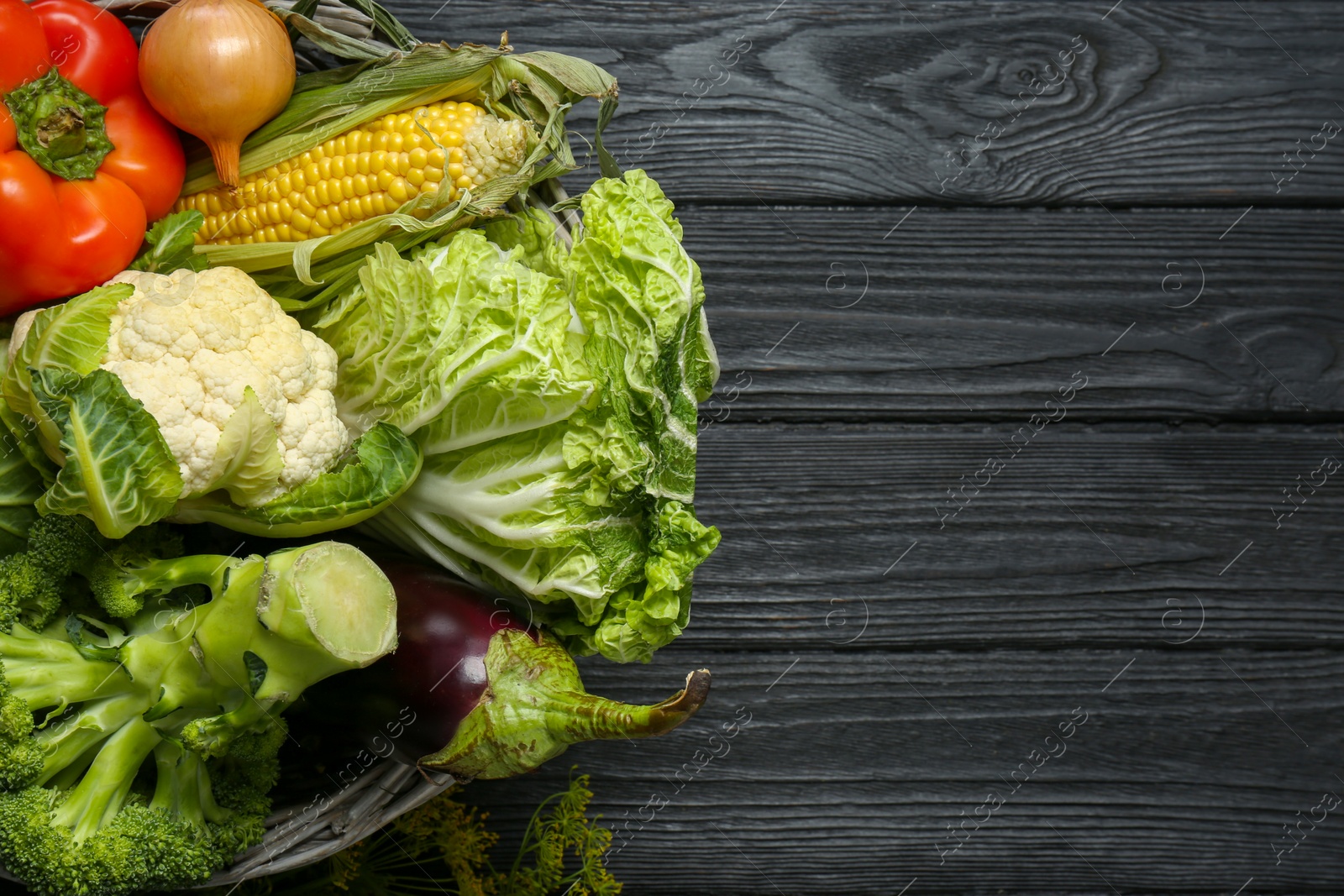 Photo of Different fresh vegetables in wicker basket on black wooden table, top view with space for text. Farmer harvesting