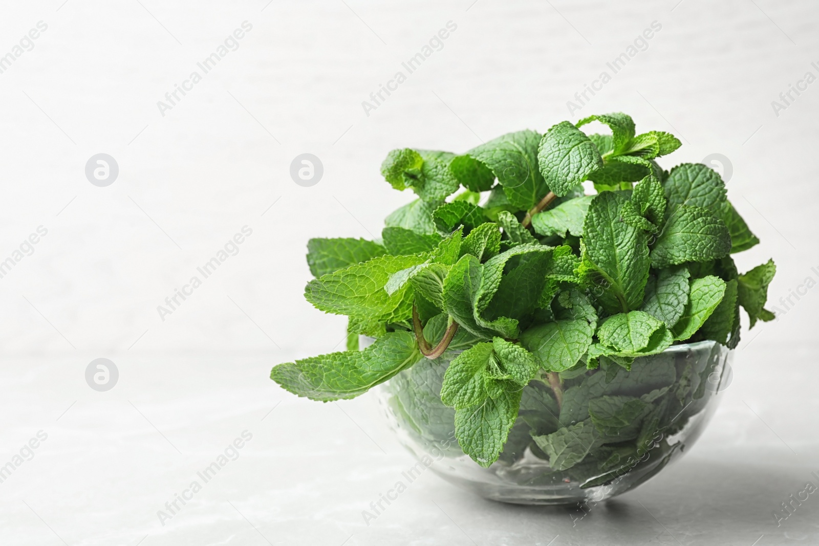 Photo of Glass bowl full of fresh green mint on light background, space for text