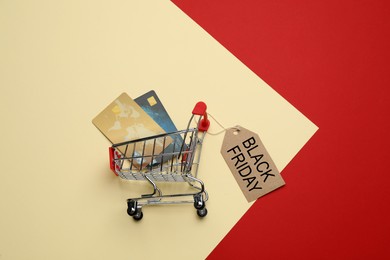 Image of Shopping cart, credit cards and tag with phrase BLACK FRIDAY on color background, flat lay