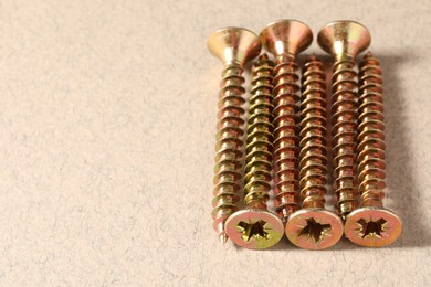 Many metal screws on beige background, closeup. Space for text