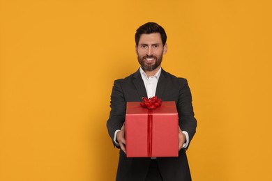 Handsome man holding gift box on yellow background