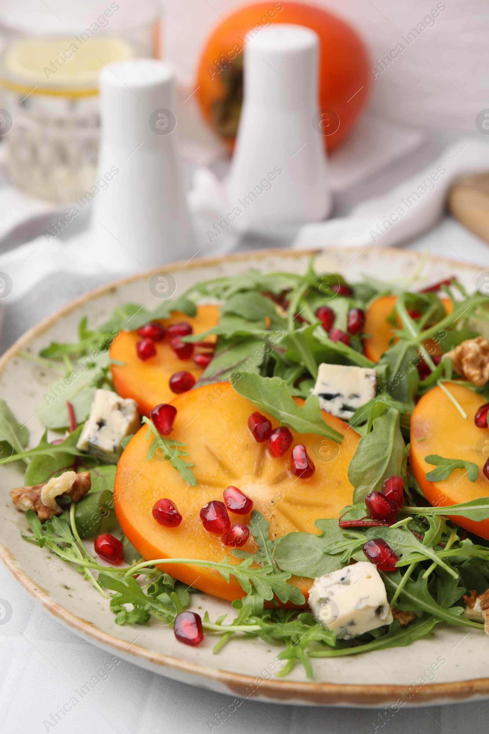 Photo of Tasty salad with persimmon, blue cheese, pomegranate and walnuts served on white tiled table, closeup