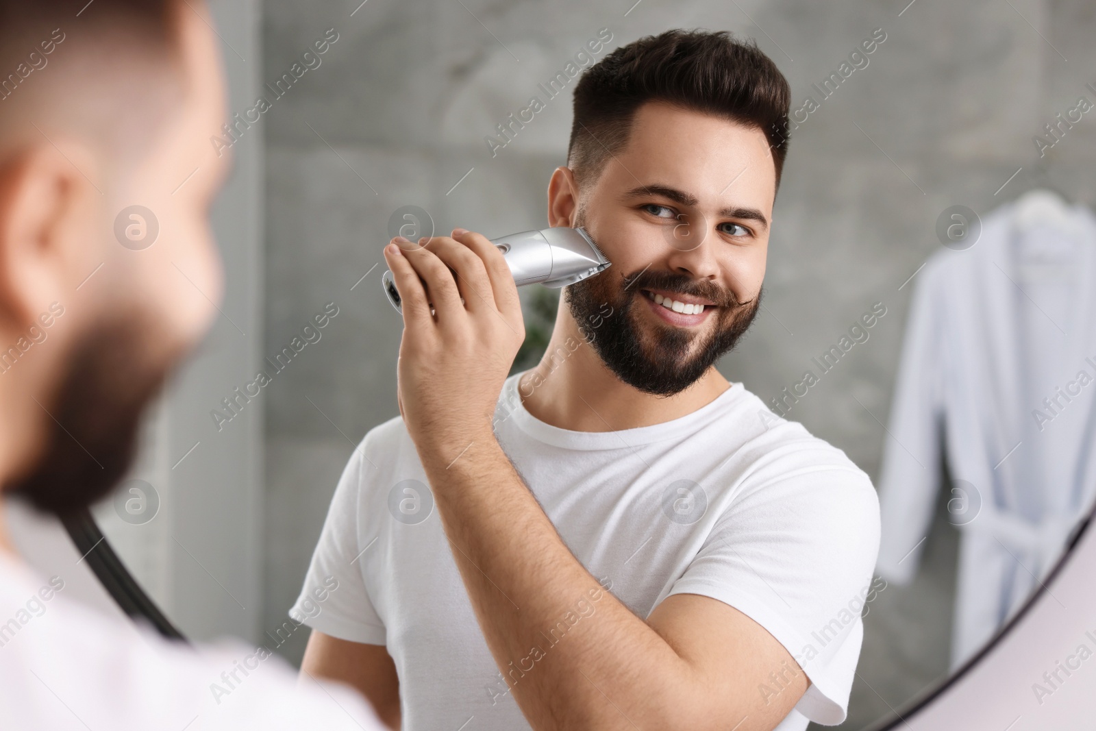 Photo of Handsome young man trimming beard near mirror in bathroom