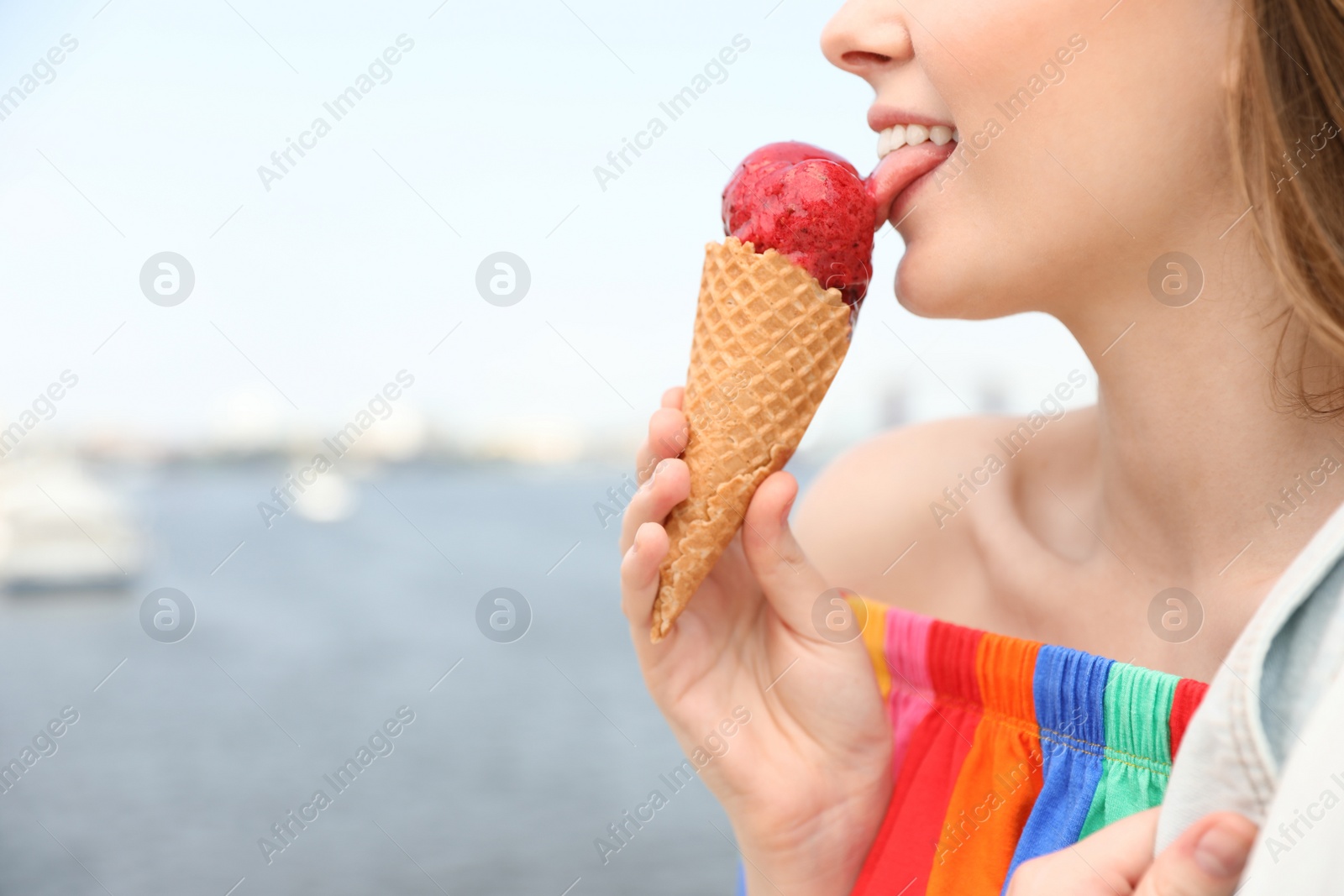 Photo of Young happy woman eating ice cream on riverside, closeup. Space for text