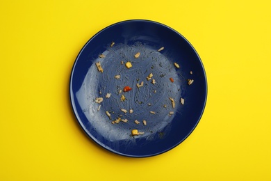 Photo of Dirty plate with food leftovers on yellow background, top view