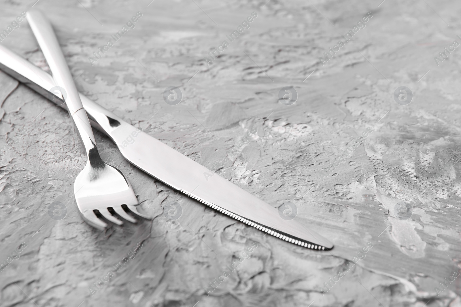 Photo of Stylish cutlery. Silver knife and fork on grey textured table, closeup