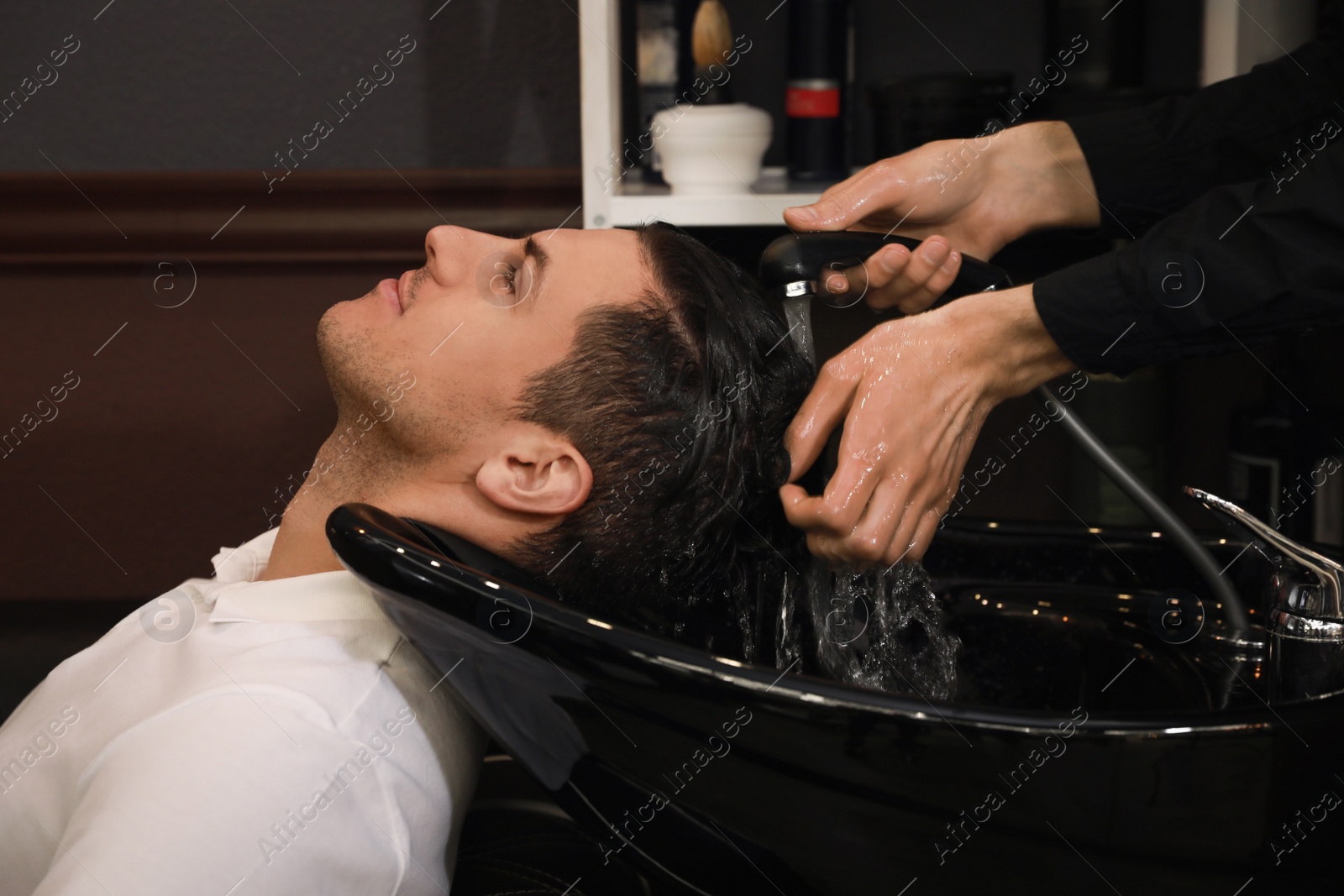Photo of Professional hairdresser washing client's hair at sink in salon, closeup