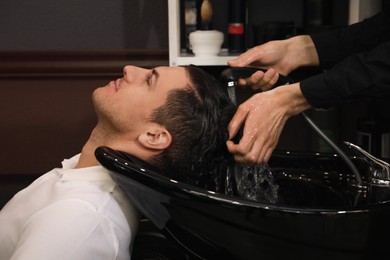 Photo of Professional hairdresser washing client's hair at sink in salon, closeup