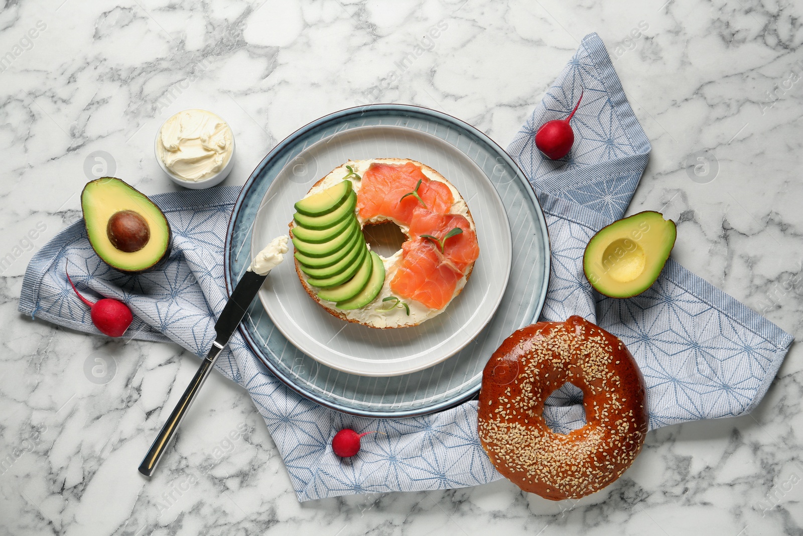 Photo of Delicious bagel with cream cheese, salmon and avocado on white marble table, flat lay