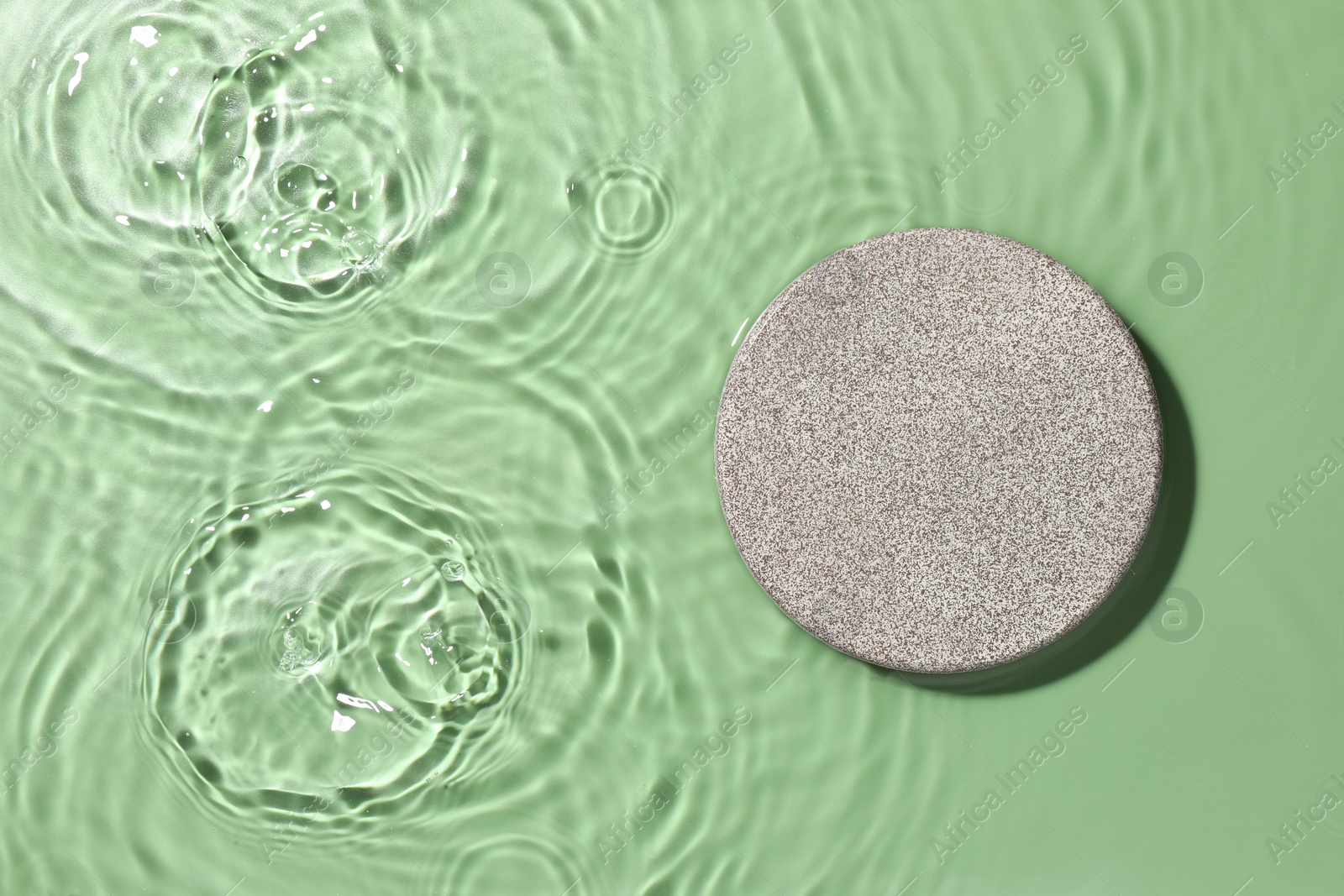 Photo of Presentation of product. Stone podium in water on green background, top view. Space for text