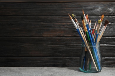 Jar with paint brushes on table against wooden background. Space for text