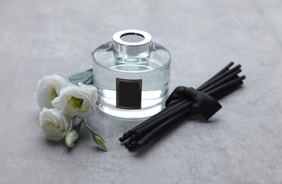 Photo of Reed sticks, glass bottle with aromatic liquid and eustoma flowers on gray marble table