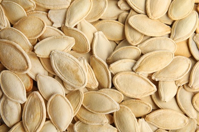 Photo of Raw unpeeled pumpkin seeds as background, top view