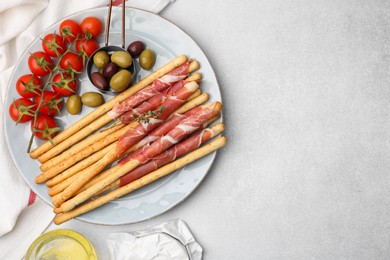 Delicious grissini sticks with prosciutto and snacks on white table, flat lay. Space for text