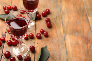 Photo of Delicious cherry wine with ripe juicy berries on wooden table. Space for text
