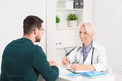 Doctor with pen and clipboard consulting patient at table in clinic