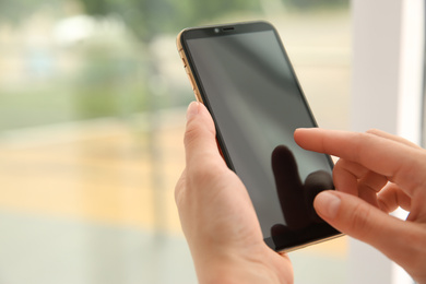 Woman working with modern smartphone indoors, closeup. Space for design