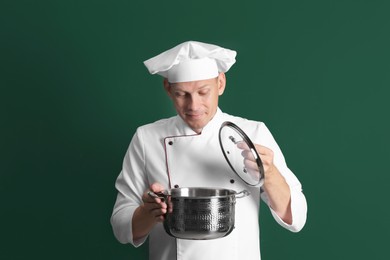 Photo of Happy male chef with cooking pot on dark green background