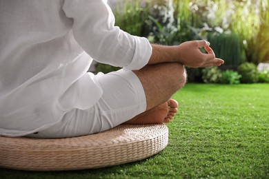 Photo of Young man meditating on straw cushion outdoors, closeup