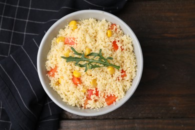 Photo of Tasty couscous with pepper, corn and arugula in bowl on wooden table, top view