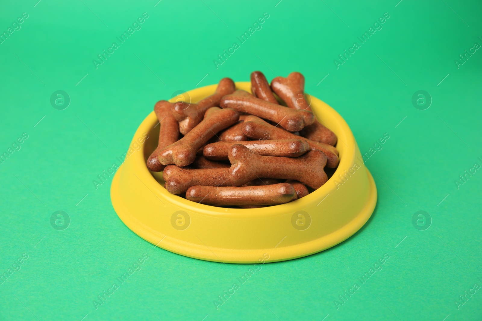 Photo of Yellow bowl with bone shaped dog cookies on green background