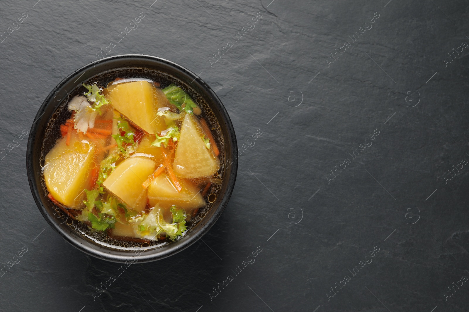 Photo of Bowl of tasty turnip soup on black table, top view. Space for text