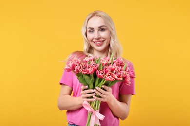 Happy young woman with beautiful bouquet on orange background