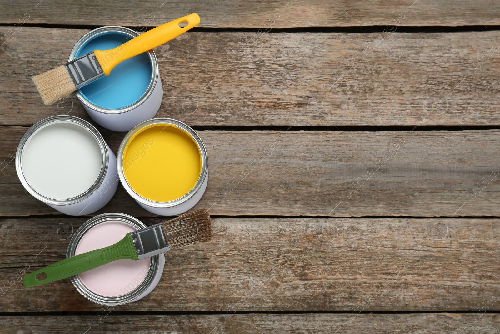 Photo of Cans of colorful paints with brushes on wooden table, flat lay. Space for text