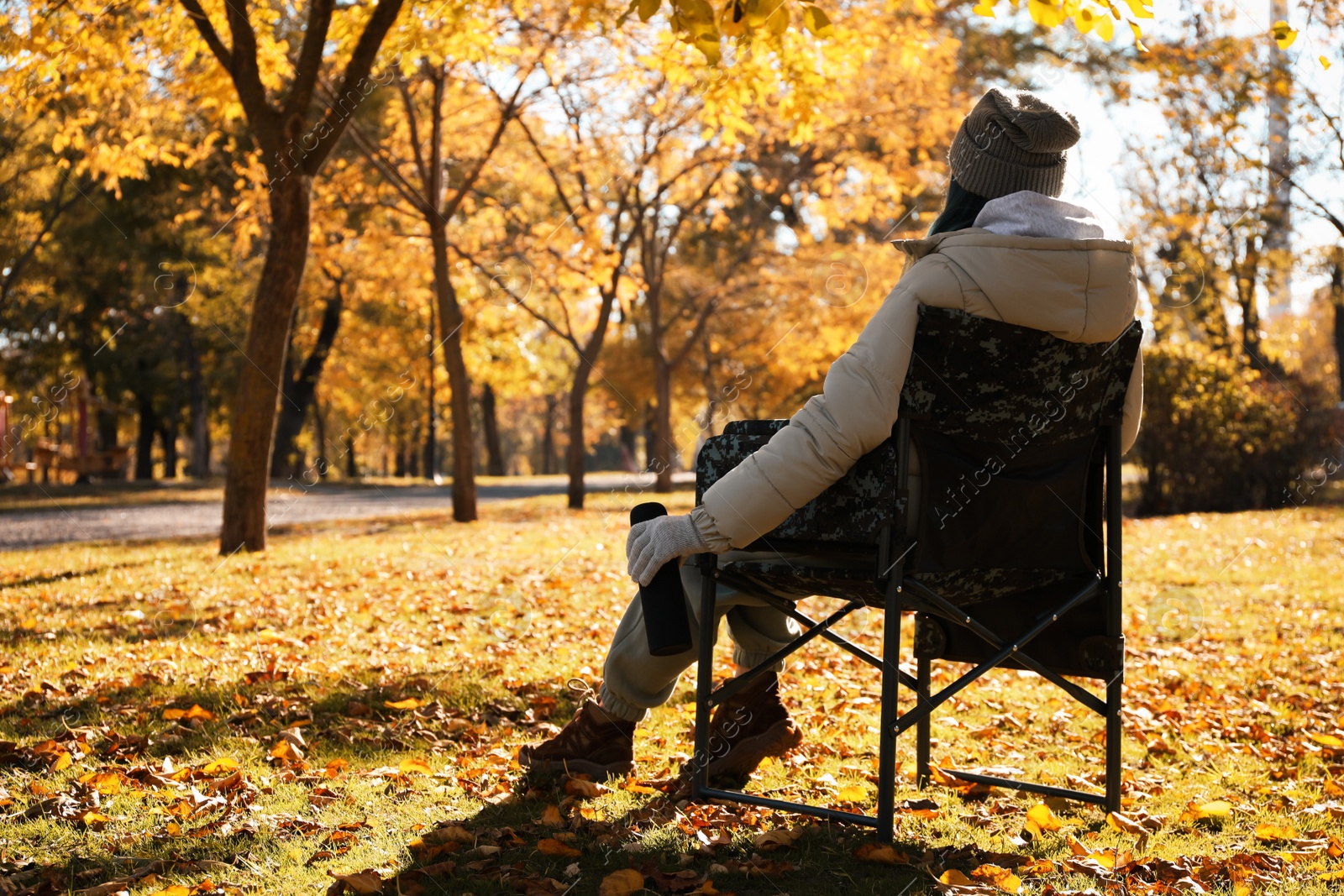 Photo of Woman with thermos sitting in camping chair outdoors on autumn sunny day