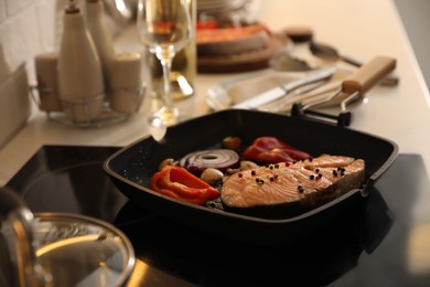 Frying pan with tasty salmon steak and vegetables on stove