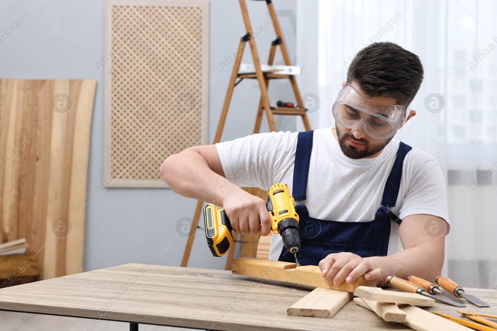 Photo of Young worker using electric drill at table in workshop