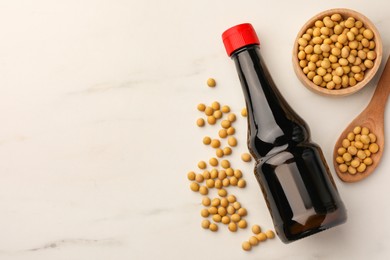 Photo of Bottle of soy sauce and soybeans on white marble table, flat lay. Space for text