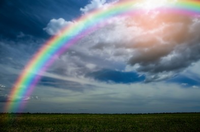 Picturesque view of green meadow and beautiful rainbow in cloudy sky